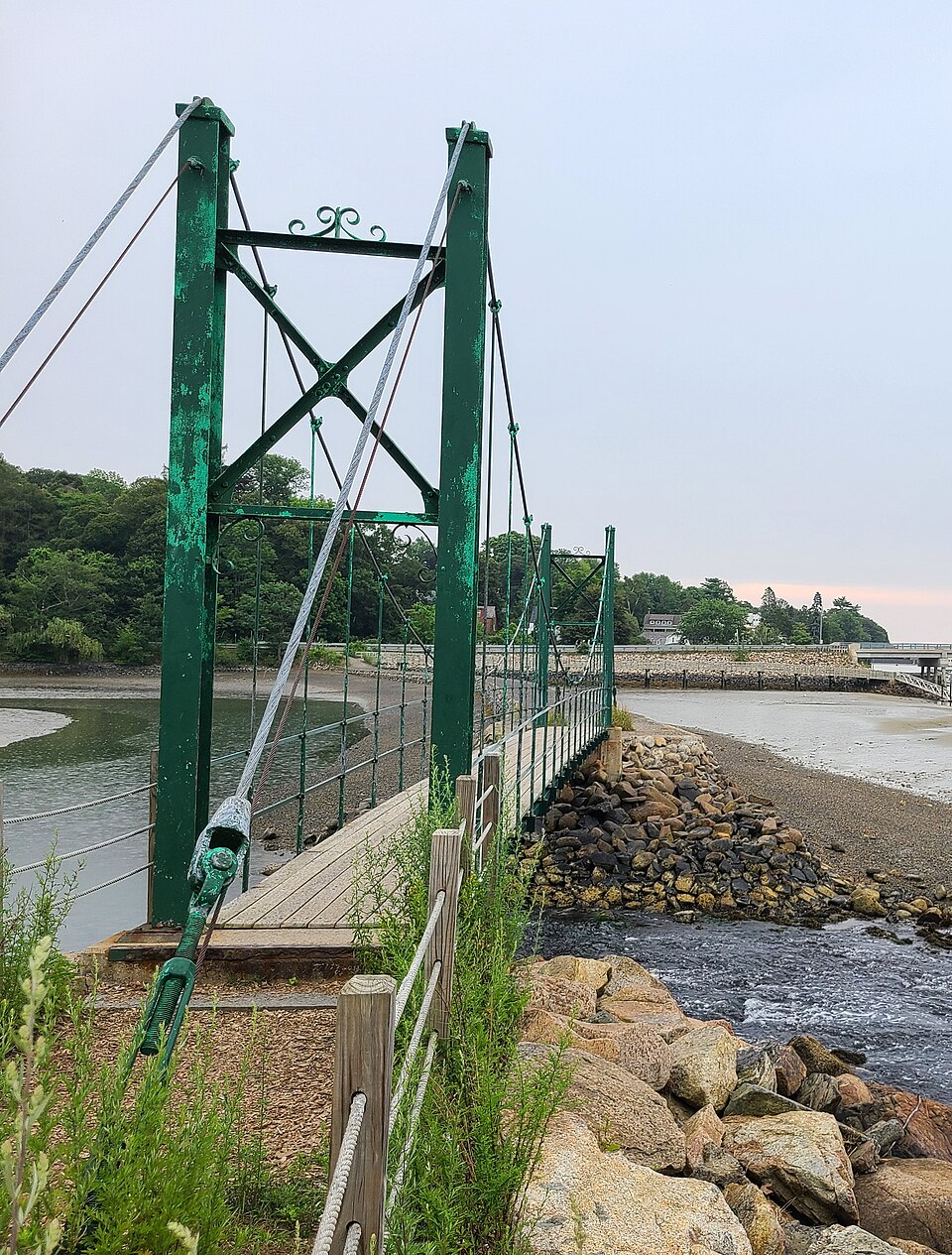 The green steel Wiggly Bridge footbridge crossing the tidal creek in York, Maine, with the York River beyond it